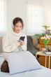 © Pichsakul - Young asian women in sweater wearing headphone and surfing entertainment with listening music on smartphone while relaxation and doing activity for spending time with slow life lifestyle at home