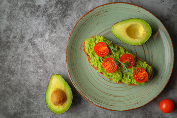 Vegan sandwich with avocado and tomatoes on a plate, on a gray background