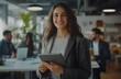 © Sagar - A smiling businesswoman stands in an office holding her tablet