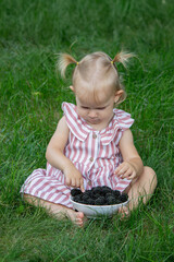 Wall Mural - little girl eats blackberry on the background of nature. Selective focus