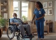 © Sagar - black nurse in blue scrubs is standing and smiling at an elderly man sitting in his wheelchair