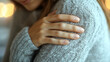 © nuupucca - Woman clutching her shoulder in a cozy sweater indicating shoulder pain