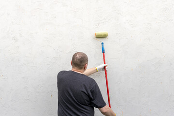 Wall Mural - A man focuses intently as he rolls paint onto a wall, bringing new life to the space in the warm glow of afternoon sunshine.