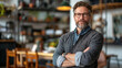 © Volodymyr - Confident middle-aged man with glasses standing with arms crossed in modern cozy workspace. Generative AI
