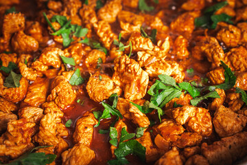 Wall Mural - The turkey, cut into small pieces, is fried in a pan in tomato sauce with parsley.