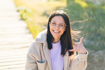 Young woman at outdoors With glasses and doing phone gesture