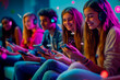 © M Jesus - Smiling teenagers enjoying music and technology in a vibrant neon-lit space.