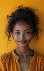 Wall Mural - A woman with curly hair and a yellow shirt is smiling. She is wearing a necklace and earrings