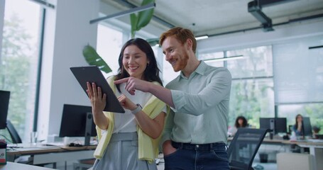 Happy young woman spending coffee break with her colleague in office. Female holding tablet device and showing something funny to her friend. People loudly laughing and enjoying positive recreation.