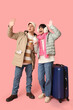 © Pixel-Shot - Beautiful young couple with suitcase and cups of coffee waving hands on pink background. Winter vacation concept