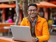 © Furqan - Happy Indian man in orange attire works on laptop outdoors