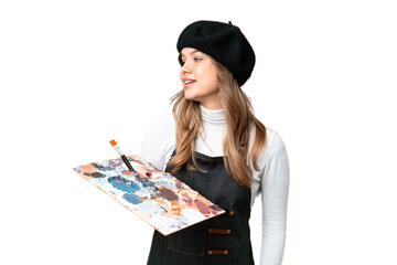 young artist girl holding a palette over isolated chroma key background looking to the side and smil