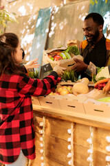 Wall Mural - Smiling African guy farmers market vendor giving fresh organic produce box to customer, selective focus. Caucasian woman buying healthy locally grown fruits and vegetables at roadside stand.