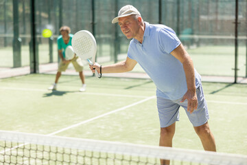 Wall Mural - Portrait of sporty senior man playing padel on open court on autumn day, ready to hit ball. Health and active lifestyle concept