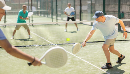 Wall Mural - Adult and elderly men paddle tennis doubles players play against two men on tennis court