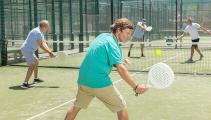 Men play padel on an outdoor tennis court. Hitting the ball with a racket