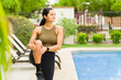 © AntonioDiaz - Fit woman in athletic clothing doing a leg stretch by the pool at a sunny tropical resort