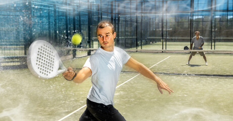 Wall Mural - Young athletic man playing padel tennis on tennis court blurred background