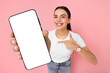 © New Africa - Happy woman pointing at mobile phone with blank screen on pink background. Mockup for design