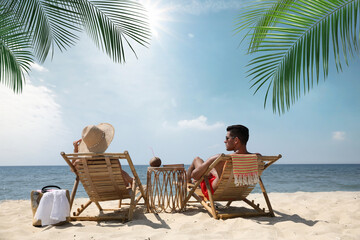 Poster - Couple relaxing on deck chairs under palm leaves on tropical beach