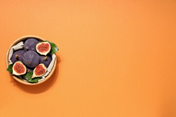 Poster - Fresh ripe figs in a wooden bowl on an orange background