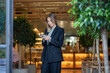 © DimaBerlin - Interested businesswoman stands with smartphone look at screen reads email, message, examines coffee shop development proposals. Focused serious female owner cafe consider offers in phone for business