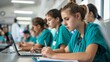 © Korawan - A group of young women in green scrubs are sitting at a table with laptops