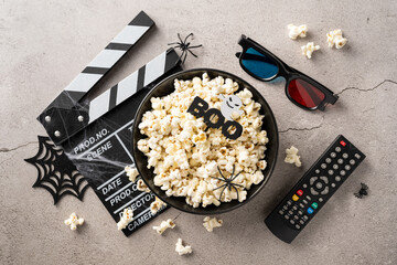 Bowl of popcorn with Halloween decorations, movie clapperboard, 3D glasses, and remote control for a spooky movie night