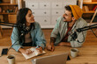© La Famiglia - Beautiful woman and man smiling as they chat into microphones during a podcast session