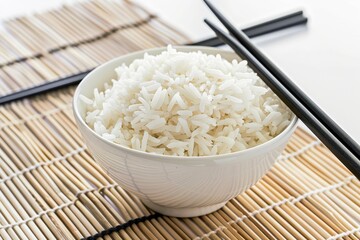 Wall Mural - White bowl of organic basmati jasmine rice with black chopsticks on bamboo mat white background