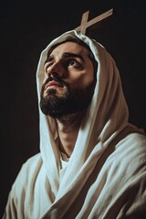 Young religious man wearing a hooded cloak holding a cross and praying