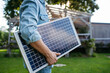 © Halfpoint - Man looking at solar panel in arms, standing in garden. Sustainable lifestyle and green household.