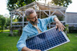 © Halfpoint - Man looking at solar panel in arms, standing in garden. Sustainable lifestyle and green household.