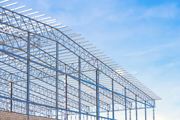 Wall Mural - Metal roof beam and columns of large industrial factory building structure in construction site against blue sky background, low angle and perspective side view