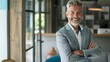 © JINGWEN - Smiling handsome businessman with crossed arms in modern office, middle-aged gray-haired man exuding confidence, business success concept.