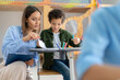 © Home-stock - Cheerful young woman teacher explaining to latin male student grammar rules, sitting near boy desk, classroom interior