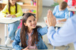 © Home-stock - Teacher giving high five to smiling European girl, sitting in classroom at desk, woman supporting female child student