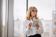 © gzorgz - Blond haired businesswoman standing in a modern office and holding a touchpad in her hand