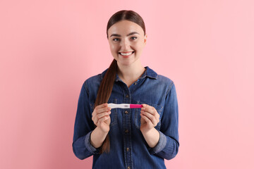 Sticker - Happy woman holding pregnancy test on pink background