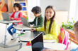 © Home-stock - Cheerful schoolgirl using laptop computer, learning online with classmates sitting at desks in modern classroom. Technology and education concept