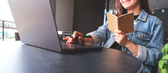 Wall Mural - Closeup image of a young woman writing on a notebook while working on laptop computer