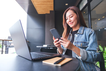 Wall Mural - portrait image of a young woman using smart phone and laptop computer in cafe