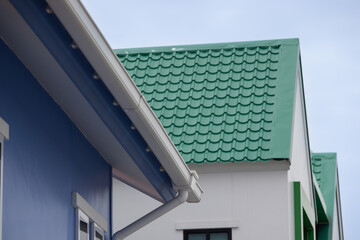 Canvas Print - A house with a blue roof and a green roof with plastic rain gutter.