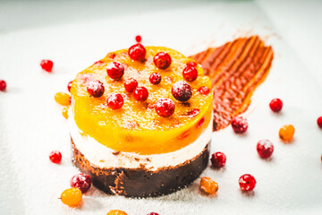 Wall Mural - Dessert or cake in layers: yellow sea buckthorn and mango jelly with lingonberries, mascarpone and chocolate shortcrust pastry on a white plate, decorated with berries and chocolate sauce.