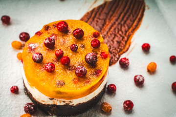 Wall Mural - Dessert or cake in layers: yellow sea buckthorn and mango jelly with lingonberries, mascarpone and chocolate shortcrust pastry on a white plate, decorated with berries and chocolate sauce.