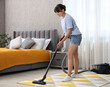 © New Africa - Young woman cleaning carpet with vacuum in bedroom