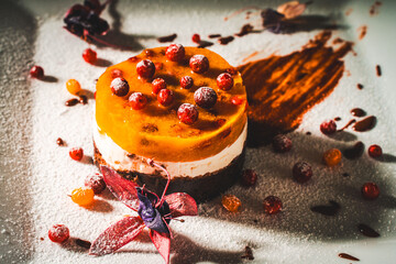 Wall Mural - Dessert or cake made of mango, sea buckthorn and lingonberry jelly with cottage cheese or cream and chocolate on a white plate decorated with flowers, berries and chocolate.