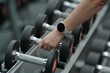 © Somkiat - Young woman wearing a sport smart watch and pulling a dumbbell off the rack in a gym.