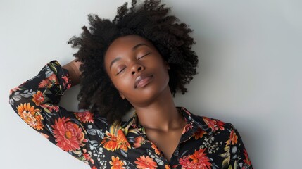 Woman with curly hair relaxing in floral shirt against a neutral background