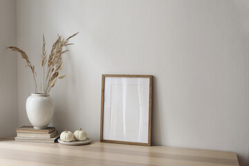 Wall Mural - Elegant neutral poster mockup. Wooden picture frame on beige table. Vase with dry grass and old books and little white pumpkins. Empty wall background. Scandinavian interior, home. Autumn decor.